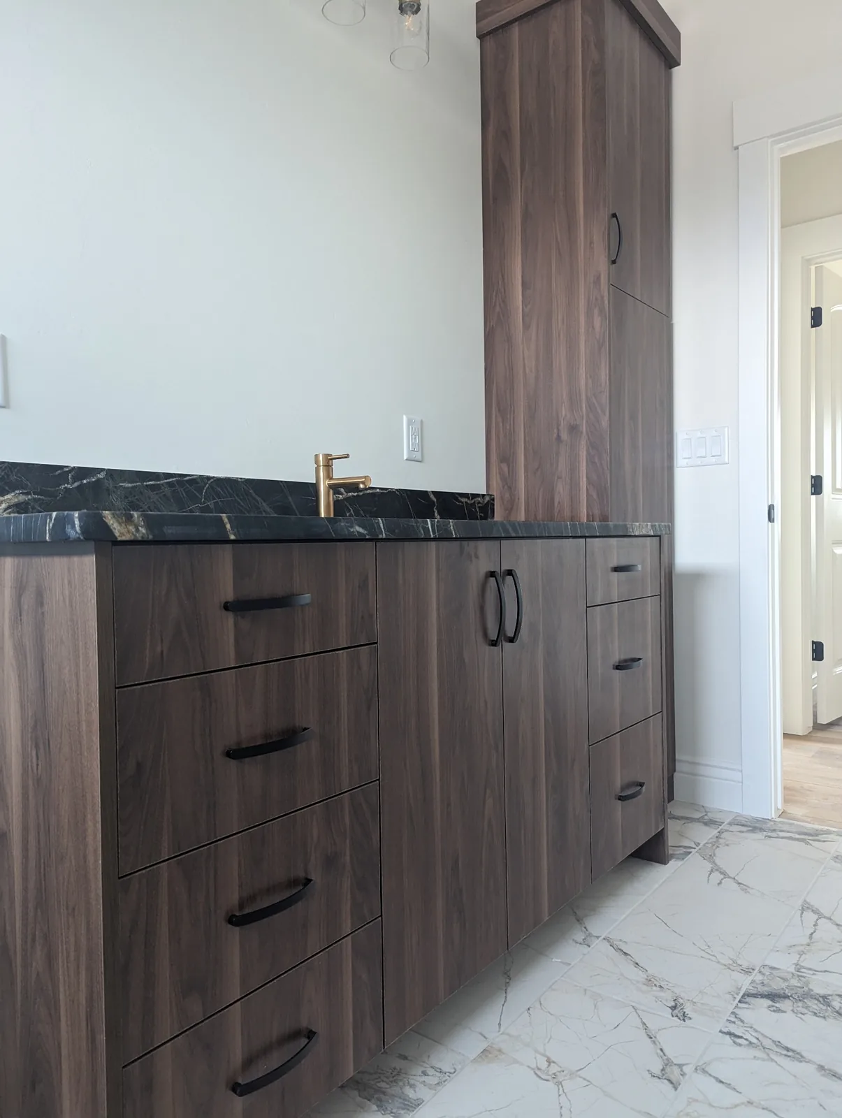 Dark woodgrain vanity cabinetry with black handles, a dark stone countertop and a tall matching cabinet.